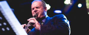 Andy Firth playing clarinet up in the air with band in background
